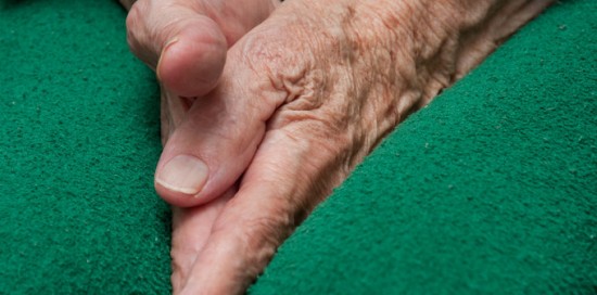 Old woman's hands tucked between her legs